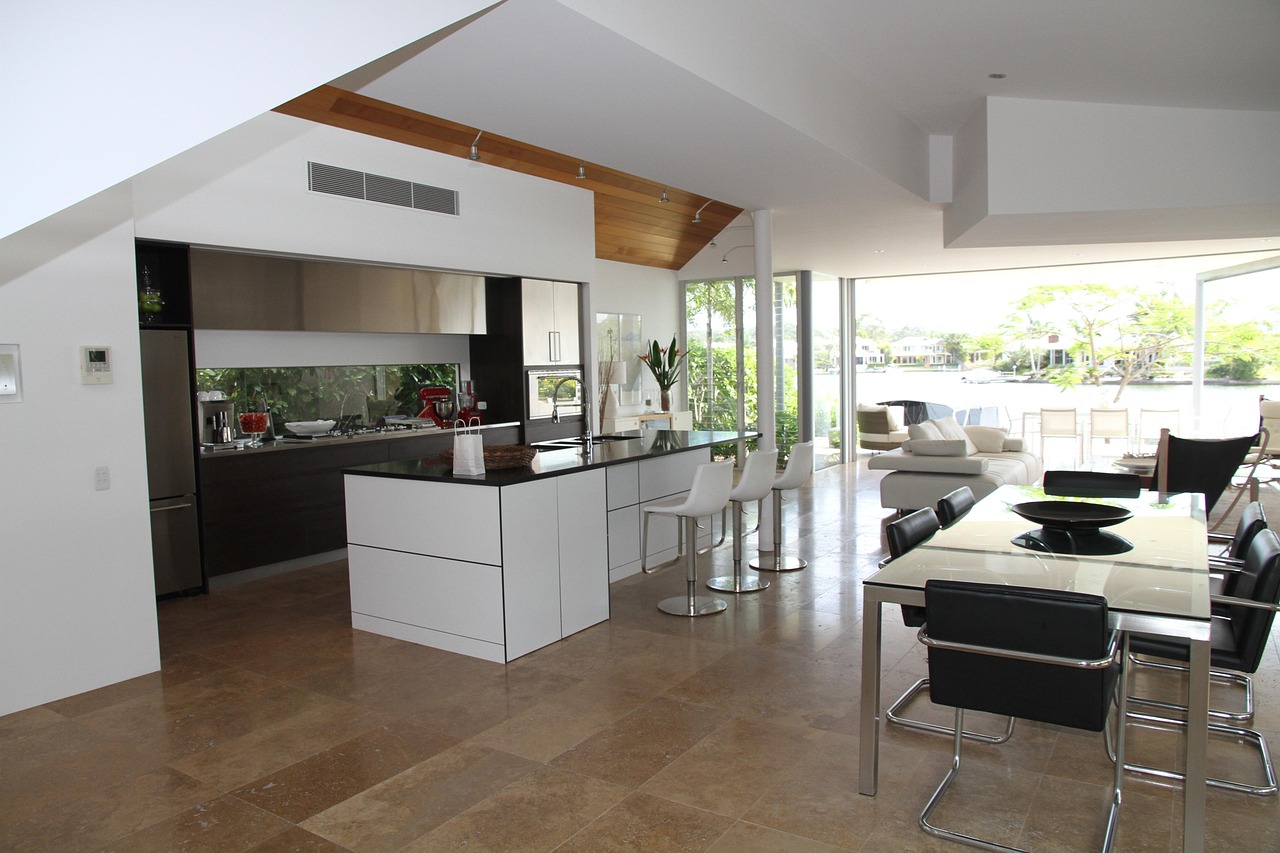 Cocina moderna abierta al salón con isla central, barra de desayunos y comedor integrado en un espacio luminoso con grandes ventanales al exterior.