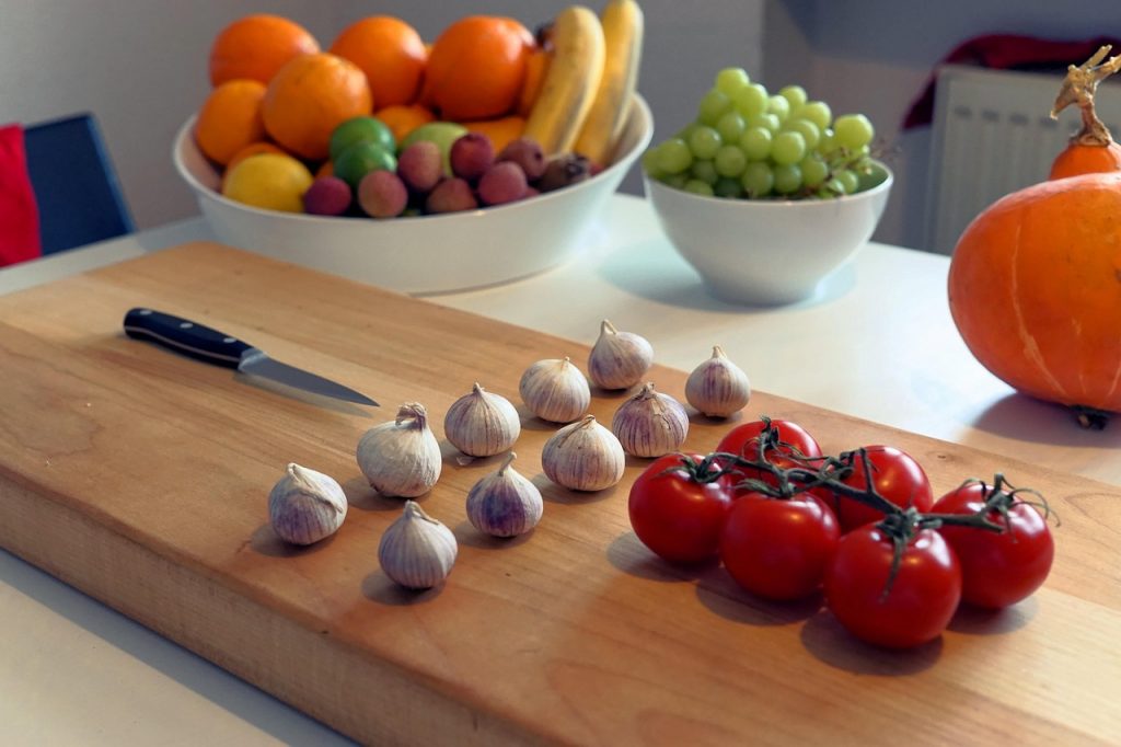 ChatGPT Plus
Tabla de madera con ajos y tomates frescos junto a un cuchillo, acompañada de un bol de frutas variadas (naranjas, plátanos, limones, uvas y kiwis) en segundo plano.
