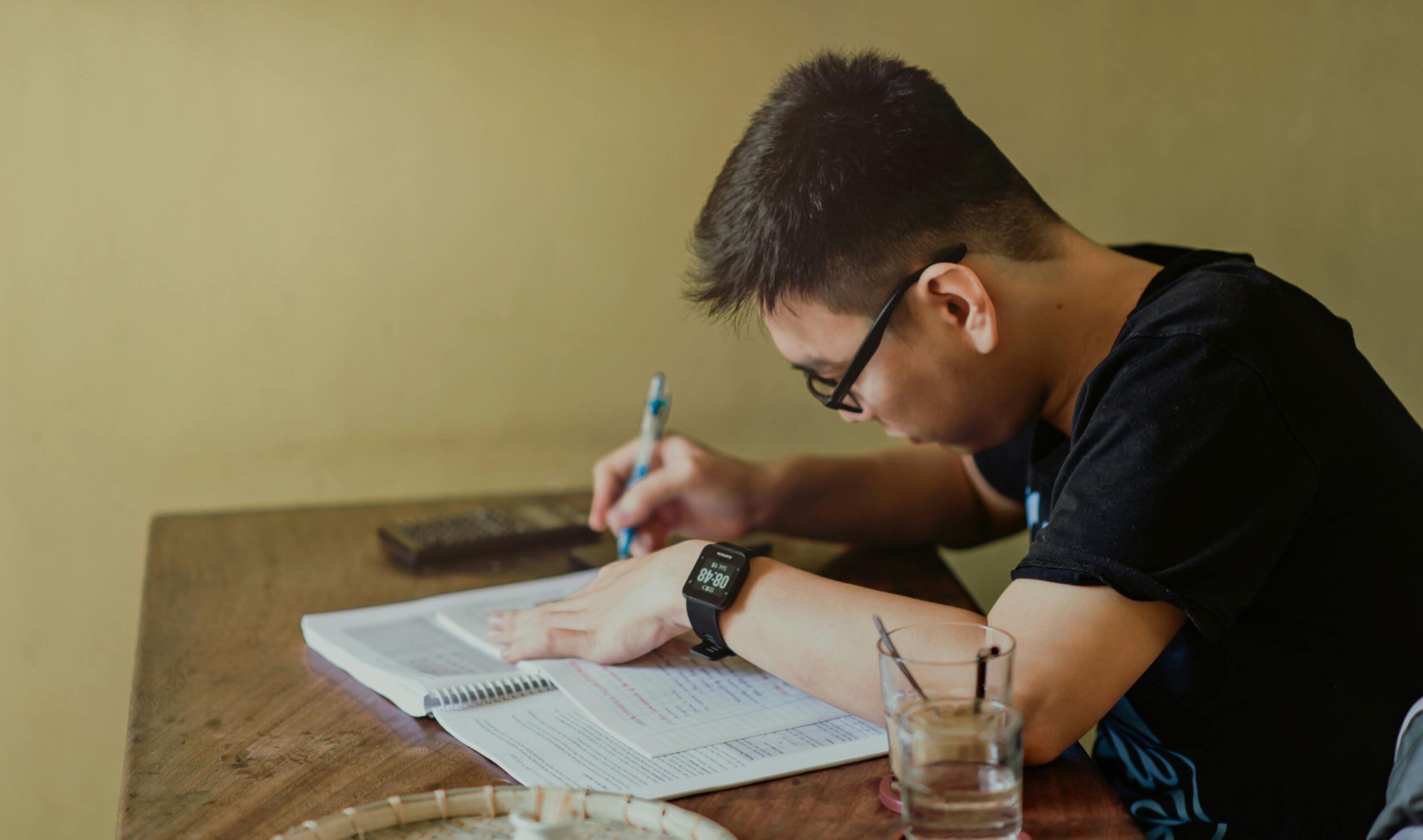 Estudiante concentrado estudiando y escribiendo en un cuaderno durante su preparación para un examen.